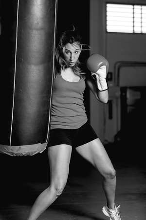 Female boxer kicking punching bag, wearing boxing gloves. Black and whiteの写真素材