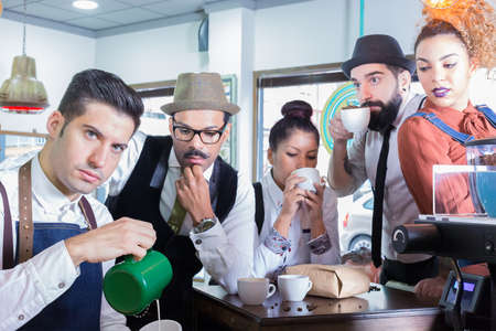 Five people in cafe drinking coffee, barista pouring milk in cup.の写真素材
