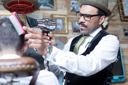 Portrait of stylish barber with moustache blow drying client's hair