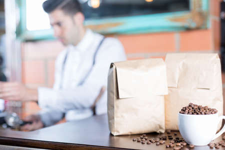 Coffee beans in cup and two paper bags, bartender unfocused on backgroundの写真素材