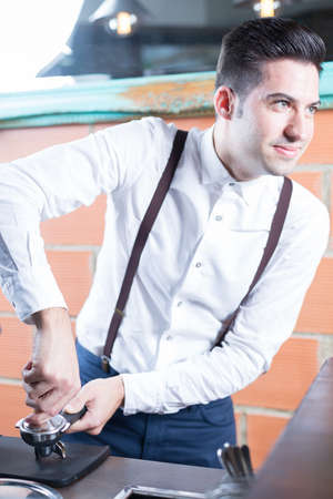 Handsome bartender pressing coffee in holder