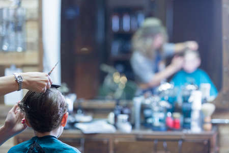 Back view of boy in barber chair. Woman cutting boy hair. Unrecognizableの写真素材