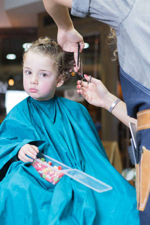 Little boy looking at camera, holding candies while sitting in barber chair