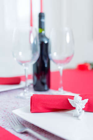 Close-up of ceramic napkin ring in form of angel against unfocused wine and glasses on background. Saint Valentines day.の写真素材