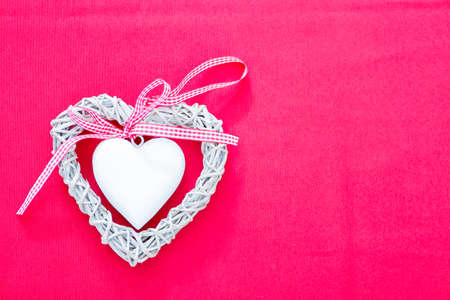 Handmade white wicker heart with checked ribbon. Pink background