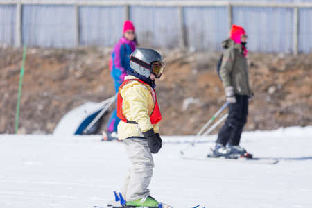 Side view of unrecognizable little boy standing on skis, wearing helmet and snow mask on a ski classの写真素材