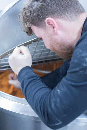 Close-up of man holding metal bar and boiling beer on a craft beer processの写真素材