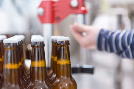 Close-up of glass bottles full of craft beer on a bottled process. Unrecognizable person on backgroundの写真素材