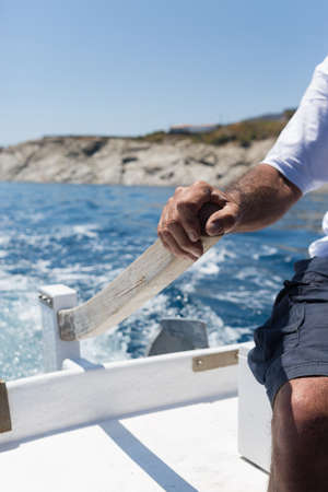Unrecognizable adult man steering white wooden boat in sunlightの写真素材