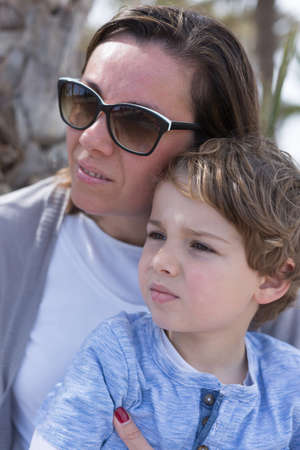 Mother in sunglasses embracing her son while both looking away outdoor.Bokehの写真素材