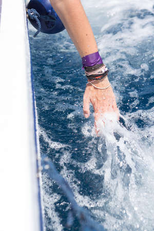 Unrecognizable woman touching splashes of foaming water while floating on yachtの写真素材