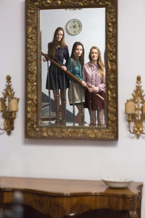 Three young elegant girlfriends standing on steps and looking in mirrorの写真素材