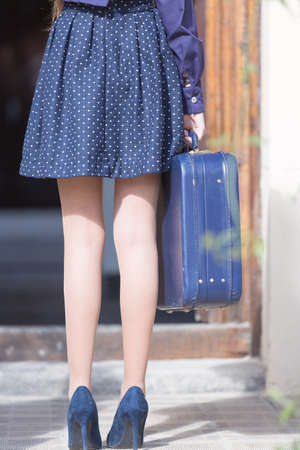 Back view of woman's legs in heels. Elegant woman holding blue suitcaseの写真素材