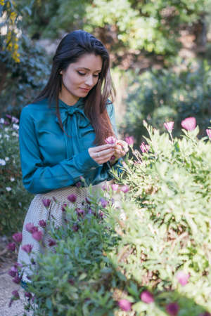 Pretty young woman with dark hair looking at violet flower in her hands. Bokehの写真素材