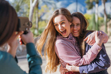 Emotional girlfriends hugging while photographer taking shotの写真素材