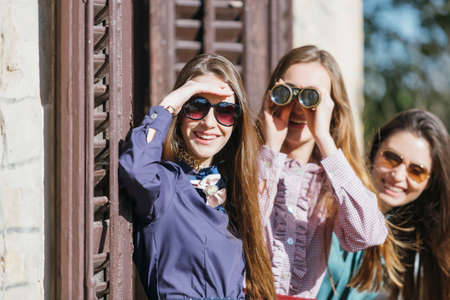 Curious girlfriends standing on balcony and spying through binoculars.の写真素材