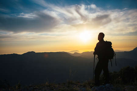 Back view of unrecognizable backpacker looking away at mountain sunset. Backlighting
