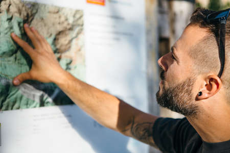 Close-up of bearded tourist looking at mountain map in sunlight