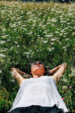 Happy adult woman in sunglasses relaxing on flower meadow in sunlightの写真素材