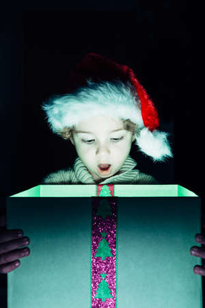 Portrait of surprised boy in Santa hat looking down at Christmas present with open mouthの写真素材