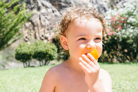 Close-up of lovely boy with curly hair eating orange outdoorの写真素材