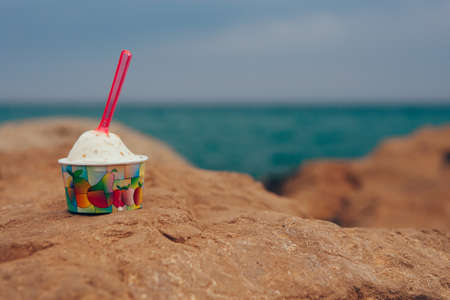 Close-up of delicious bowl of ice cream with spoon on rock against of unfocused sea. Copy space area availableの写真素材