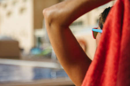 Back view of unrecognizable woman with arm up relaxing against of swimming poolの写真素材
