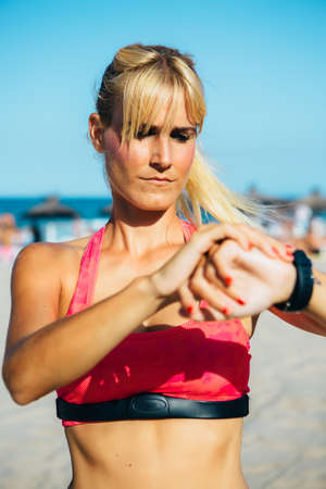 Portrait of young sportswoman checking time on watches at beachの写真素材