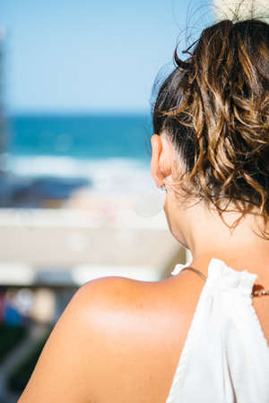 Back view of bare shoulder of brunette woman with tail against of beach and sea on blue sky.の写真素材