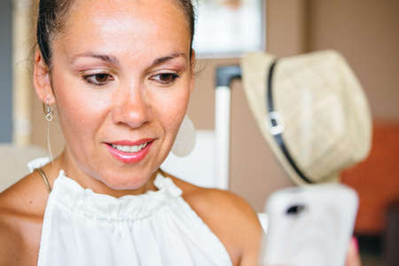 Portrait of toothy smiling woman using smartphone. Straw hat on background