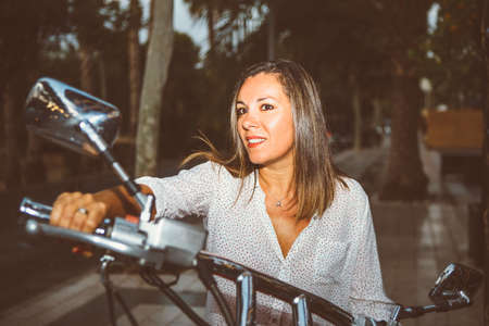 Portrait of beautiful brunette woman sitting on motorcycle in the streetの写真素材