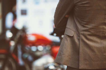 Back view of elegant man with arms crossed against unfocused motorbike at exhibitionの写真素材