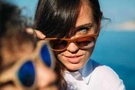 Portrait of pretty brunette girl looking at camera over sunglasses. Another woman in foreground.の写真素材