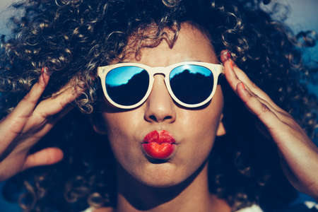 Portrait of beautiful mixed race girl with curly hair and full lips touching sunglasses on faceの写真素材