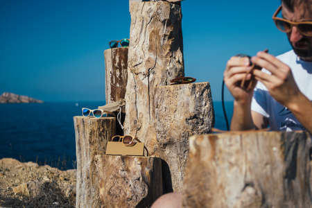 Stylish wooden sunglasses with colorful lenses lying on a wooden pedestal. Craft master on foregroundの写真素材