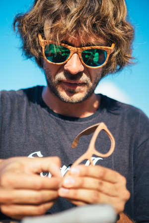 Portrait of long haired man in sunglasses sitting and crafts wooden rim glassesの写真素材