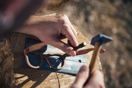 Over shoulder view of crafting handmade wooden sunglasses with hammer on workplaceの写真素材