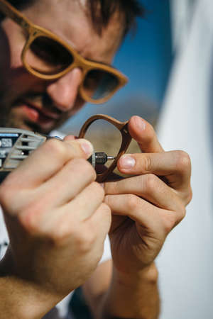 Close up of stylish craft master polishing wooden rim glasses with sanderの写真素材