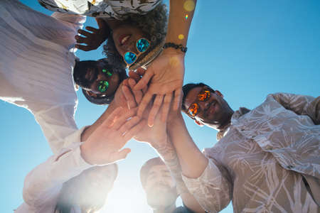 Portrait of smiling stylish friends standing in circle and folds hands togetherの写真素材