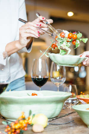 Women at celebration dinner assist each other with taking salad with cherry tomatoes. Close up view.の写真素材