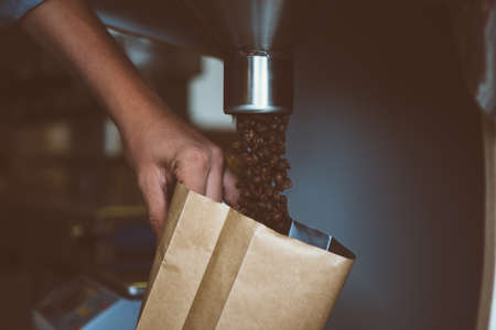 Unrecognizable worker holding bag and filling it with coffee beans