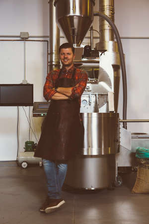 Portrait of smiling handsome worker in apron looking at camera at iron machine