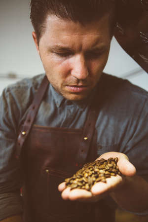 portrait of adult master of coffee looking down at roasted coffee beans in hand