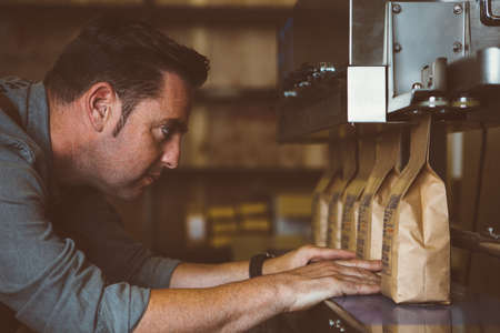 Side view of adult man looking at row of packages of roasted beansの写真素材