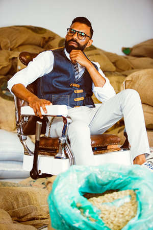 Portrait of bearded man in glasses on armchair against of textile bags with coffee beansの写真素材