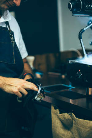 Close-up of bartender cleaning portafilter with towel beside steaming wand of coffee machineの写真素材