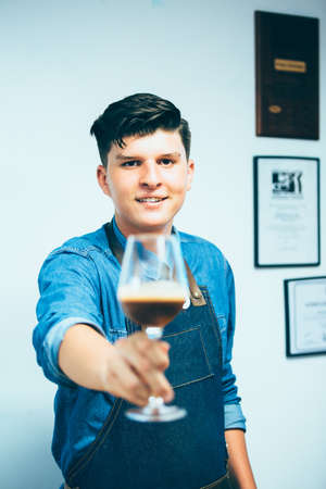 Portrait of professional young barista pulling wine glass with coffee at cameraの写真素材