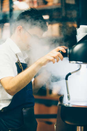 Side view of bartender in glasses turning switcher of wand in steamの写真素材