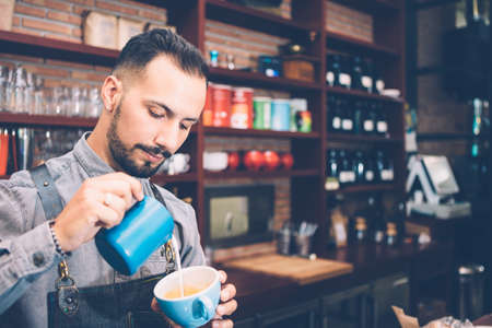 Portrait of bearded bartender preparing latte art in blue cup in cafe