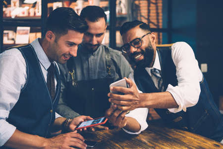 Multiracial group of friends looking at phone screen with smile at tableの写真素材